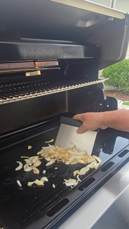 Onions being turned with a scraper on a grill griddle