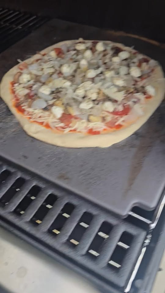 A topped pizza on a stone inside a Weber Summit grill